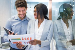 Attractive african-american businesswoman showing financial graphs to her caucasian male colleague in office.